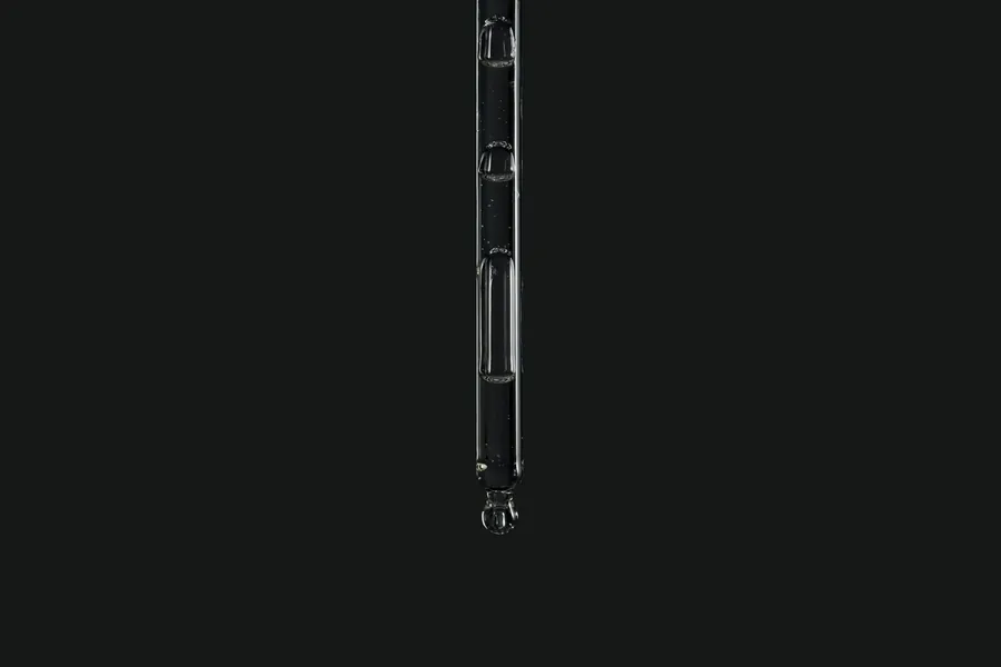 Clinique La Prairie visual for regenerative medicine: a glass pipette with a clear drop against a dark background